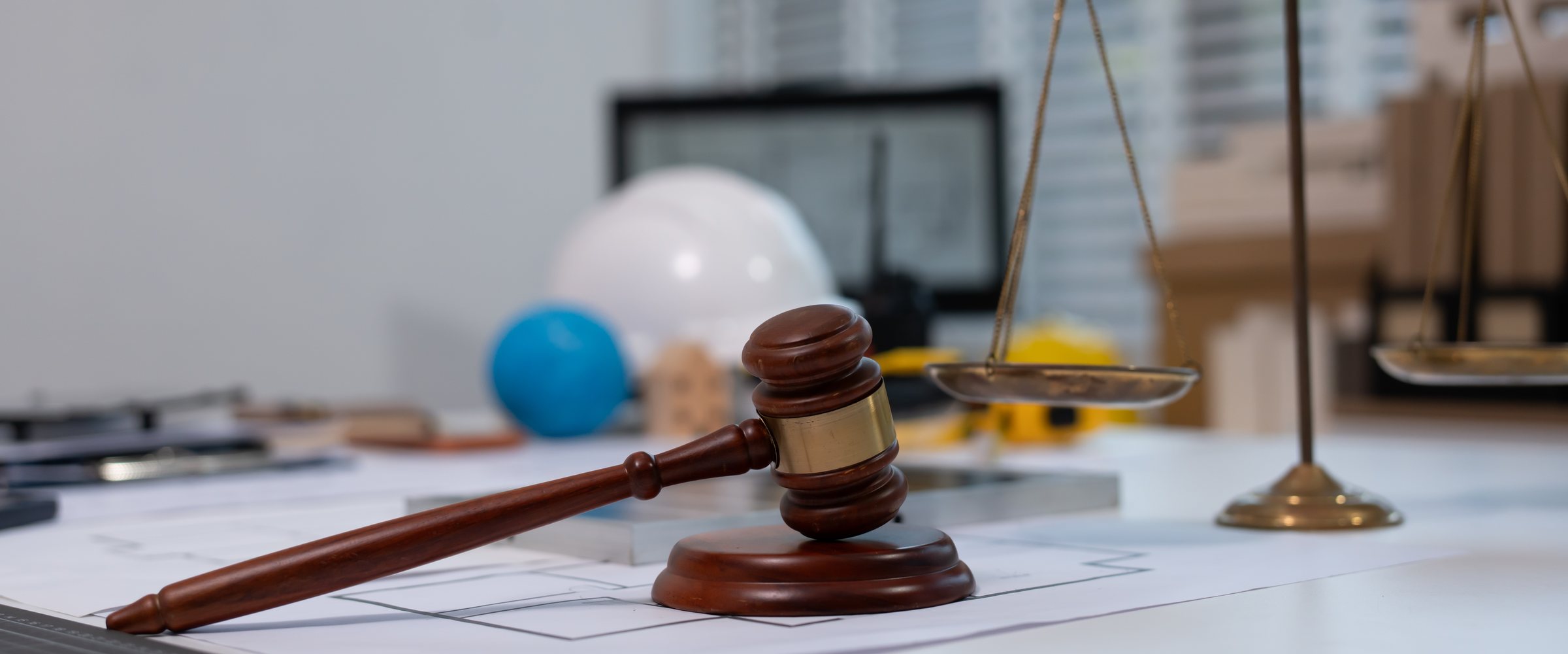 Legal office desk scene with wooden judge gavel on documents and brass scales of justice, suggesting law, court, litigation, and legal consultation in a modern 