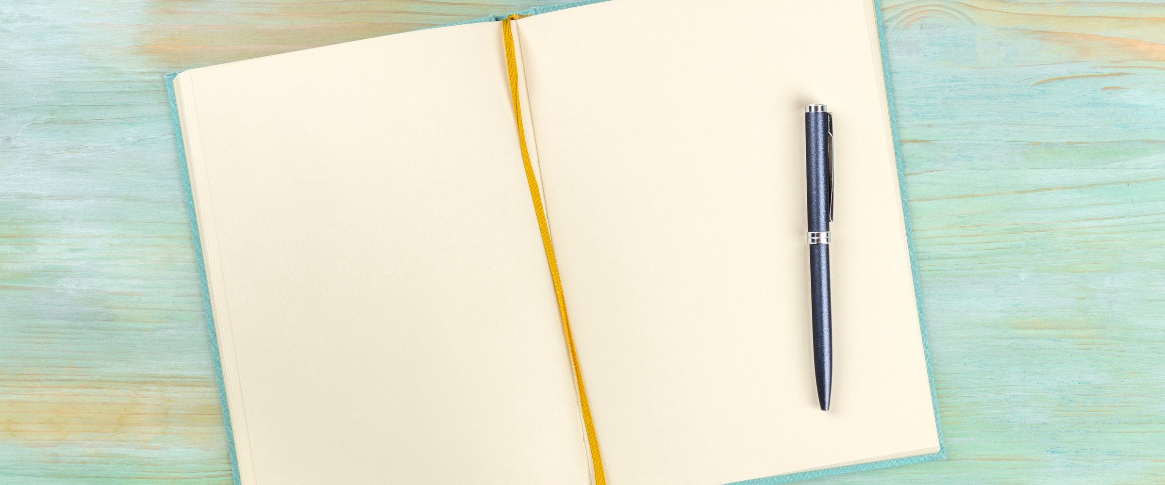 A top shot of an open journal with a pen on a teal blue background with a place for text