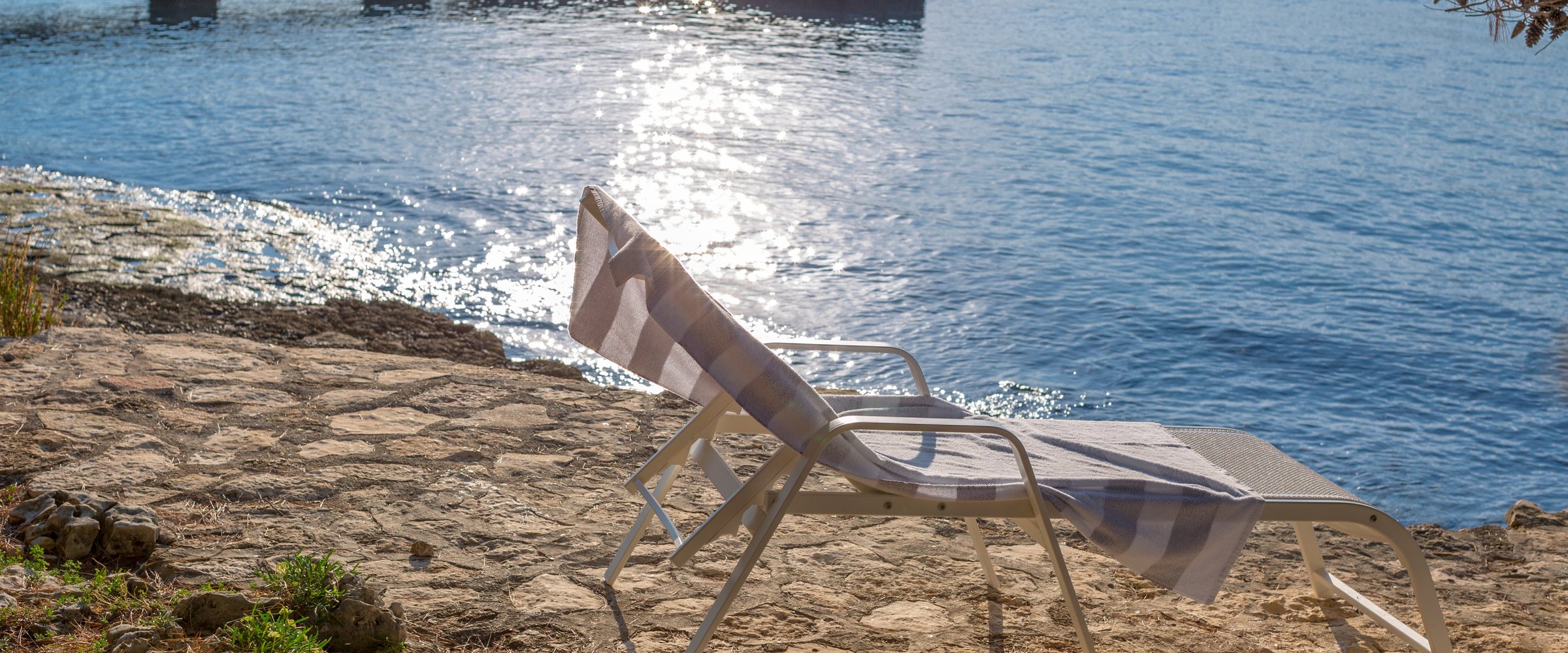 Empty lounger on the rocky beach with blue sea background