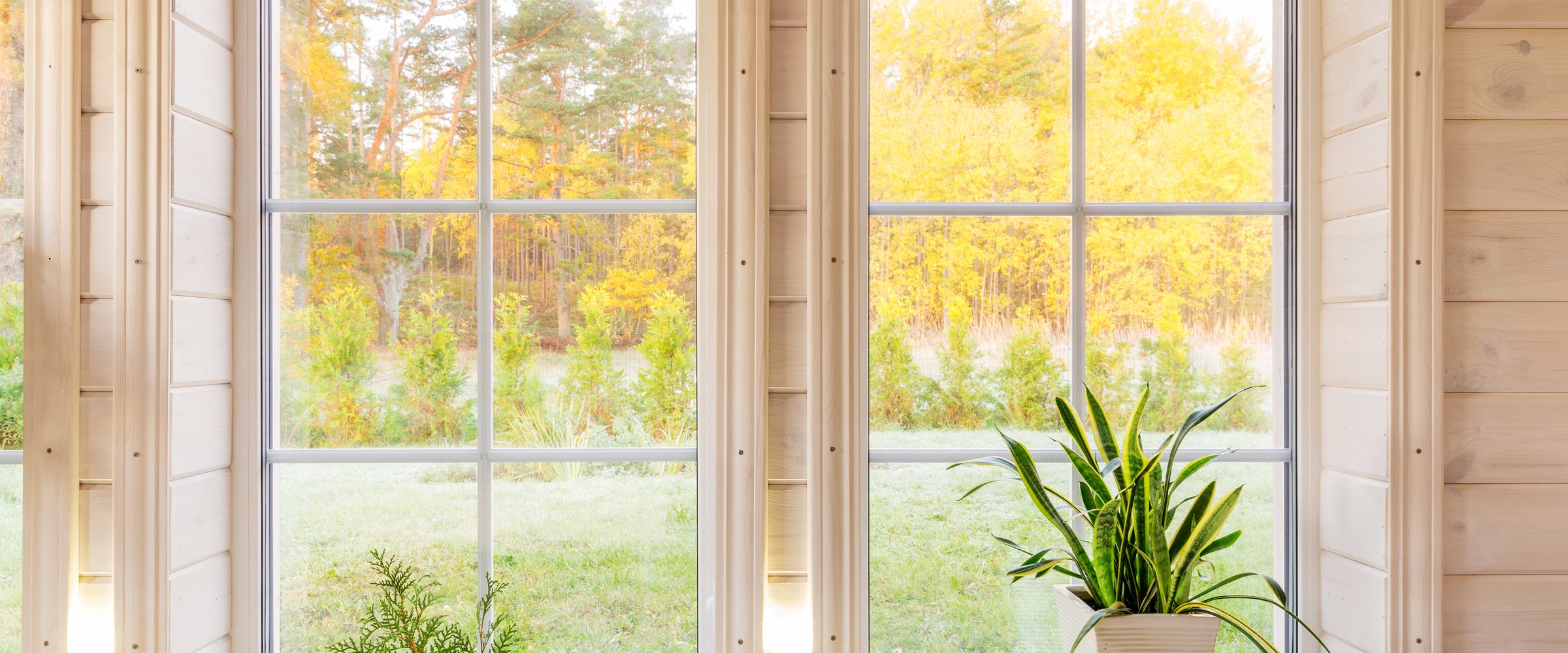 Bright interior of the room in wooden house with a large window overlooking the autumn courtyard. Golden autumn landscape in white window. Home and garden, fall