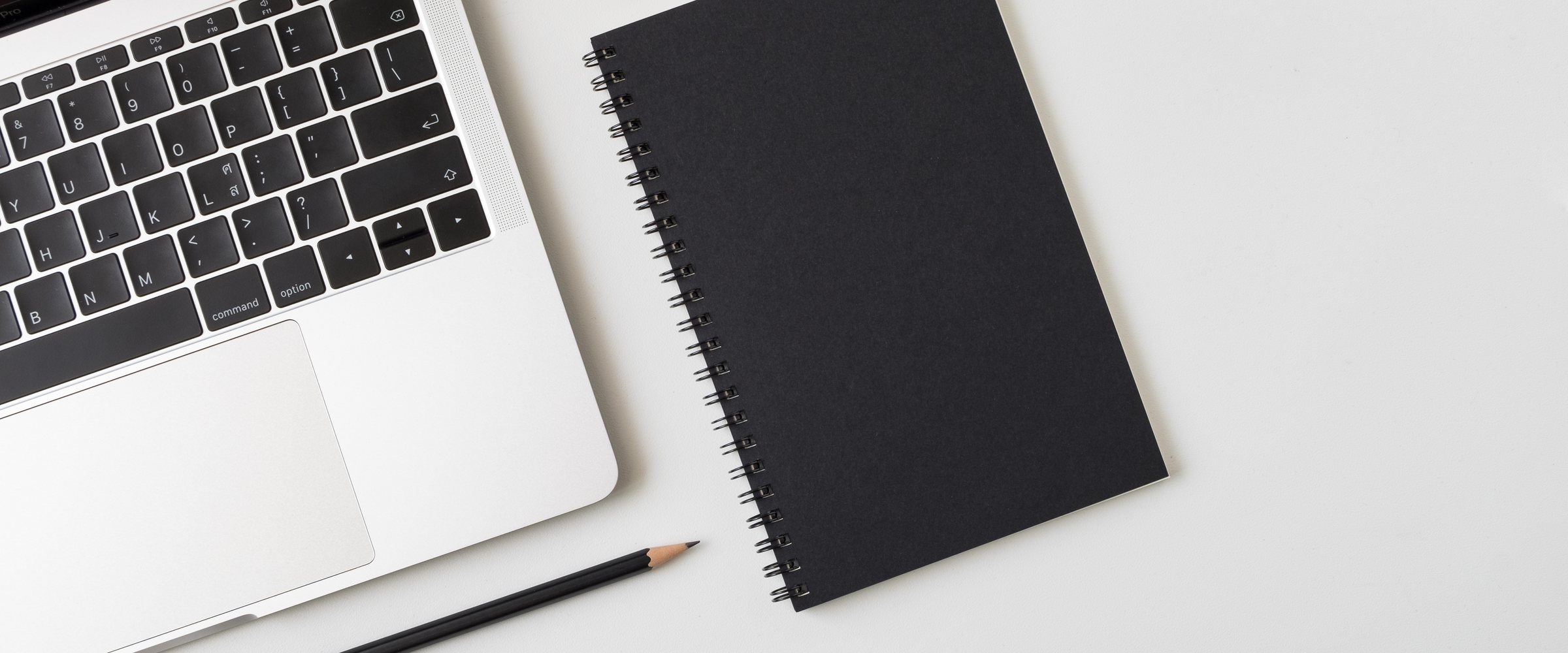 Top view desk with laptop closed black cover notebook and pencil on white desk background
