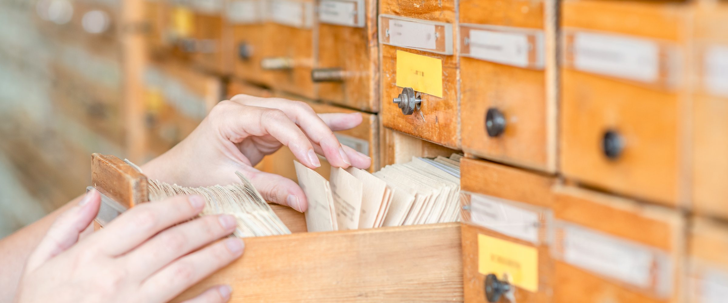 Close up hands searching cards in old wooden card catalogue
