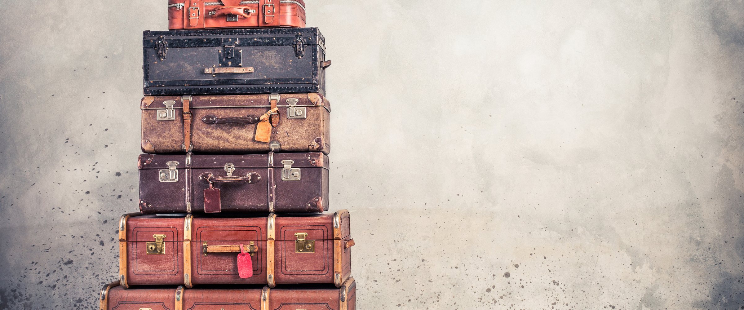 Vintage classic outdated trunks luggage with tags, old antique leather suitcases tower front concrete wall background. Travel baggage concept. Retro style filte
