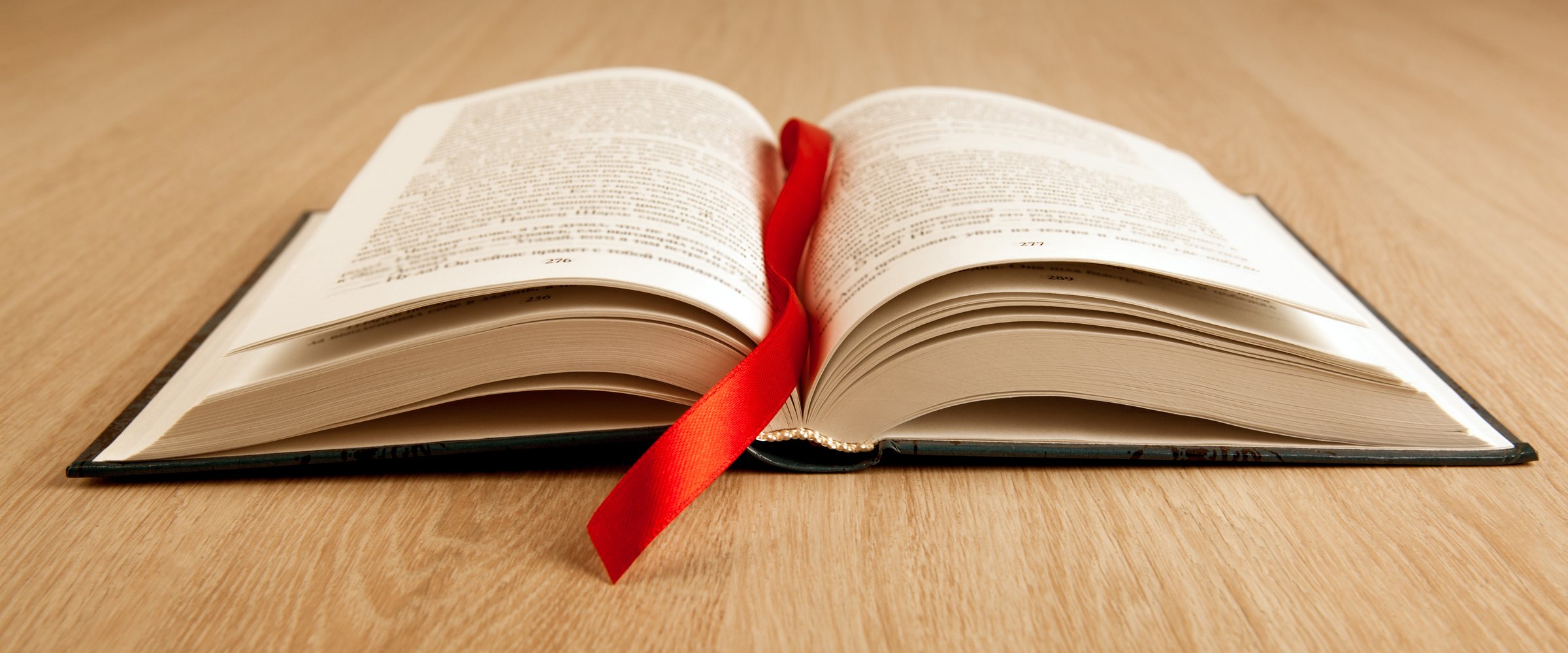 new open book on a wooden table with a red ribbon bookmark