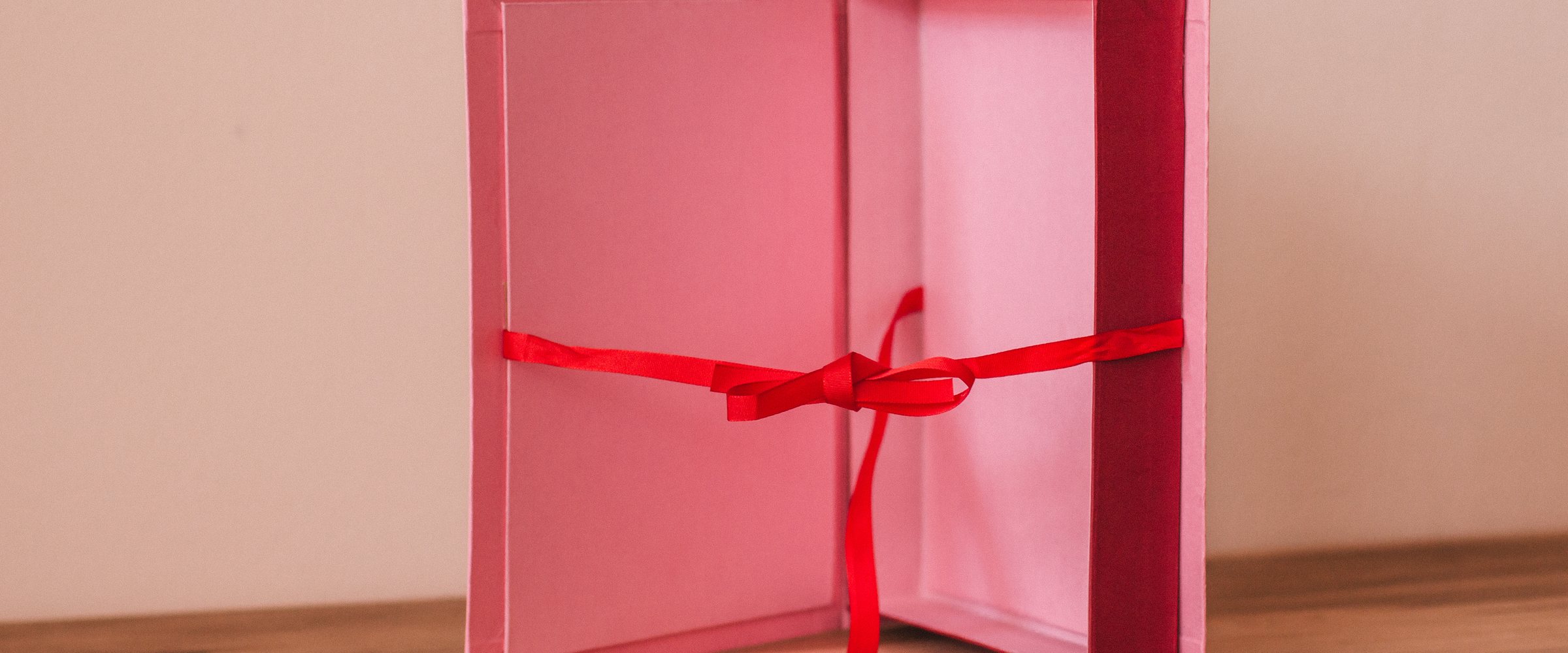 Pink wedding gift box tied with red ribbon on wooden table