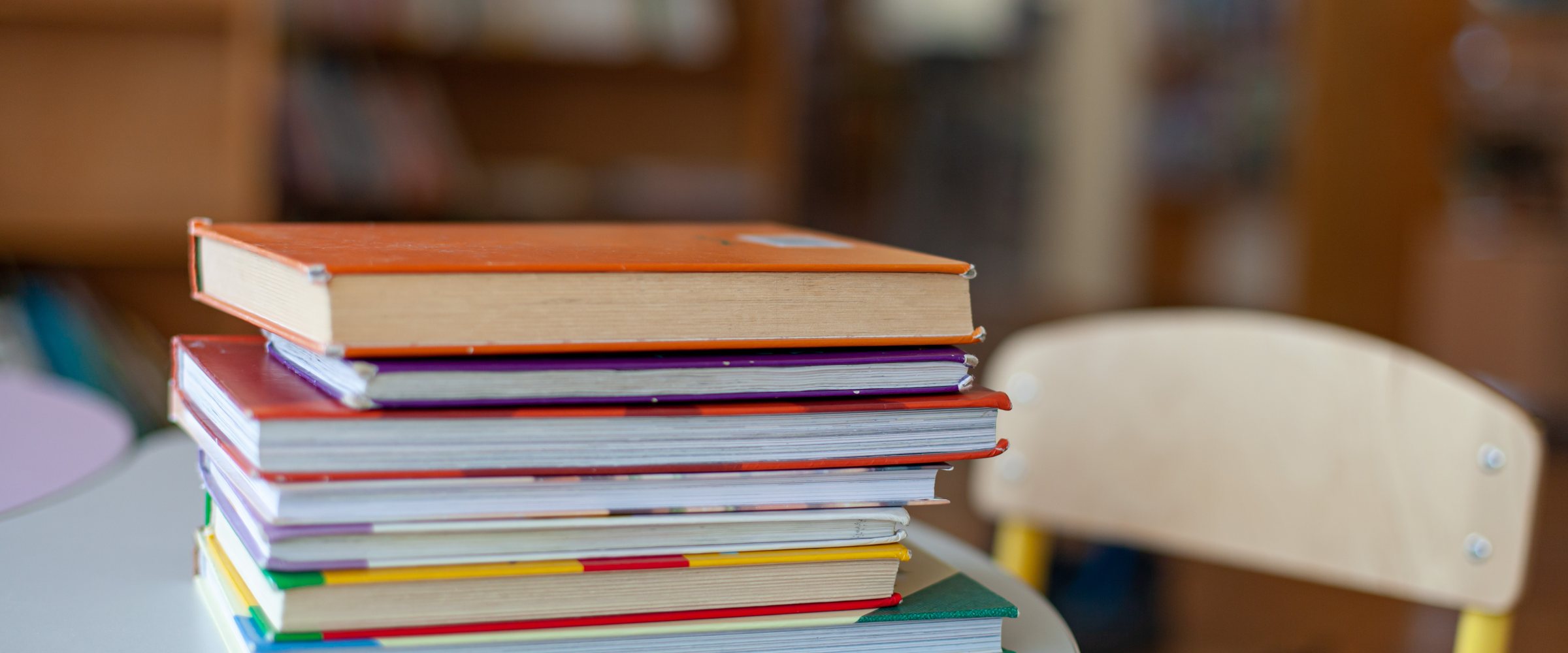 Colorful stack of hardcover books on round table in classroom or library interior. Back-to-school, study, reading and education.