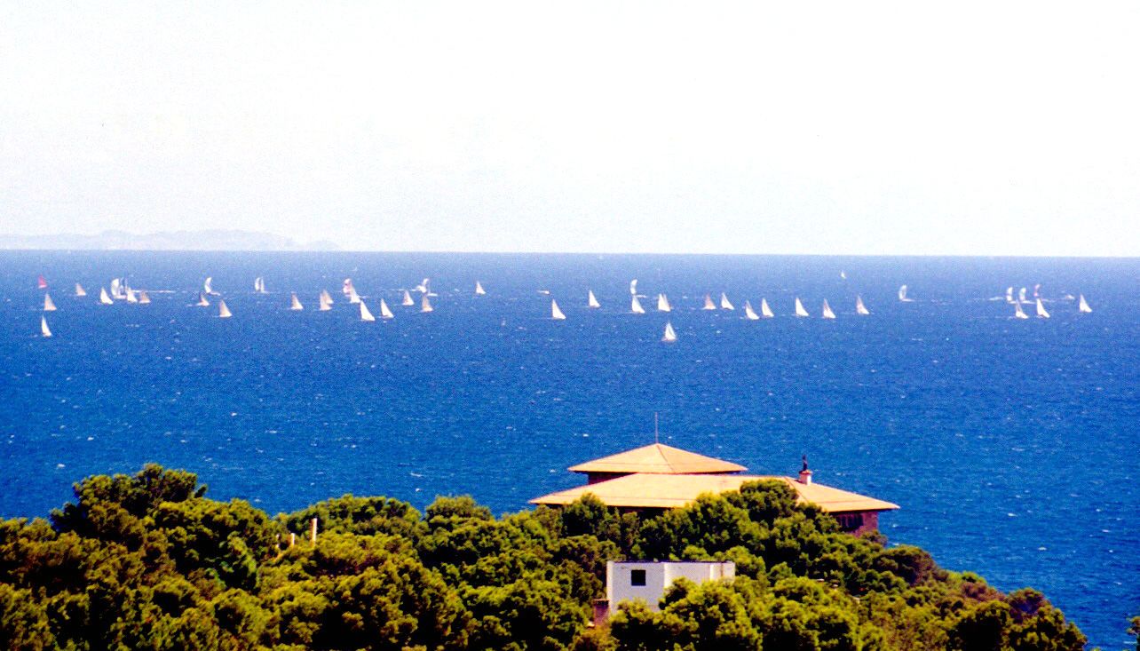 The Palace of Marivent among pine trees, with sailing yachts participating in the Trofeo Almirante Conde de Barcelona on the, Superyacht Cup Palma